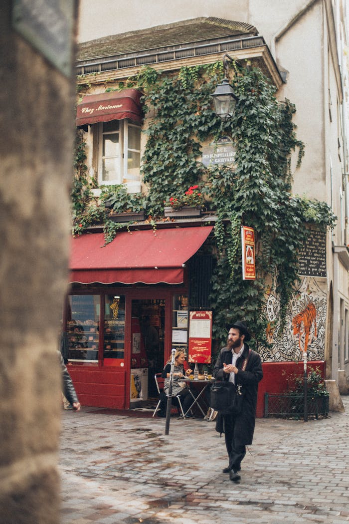 Man walking by cozy ivy-covered café on a narrow cobblestone street.