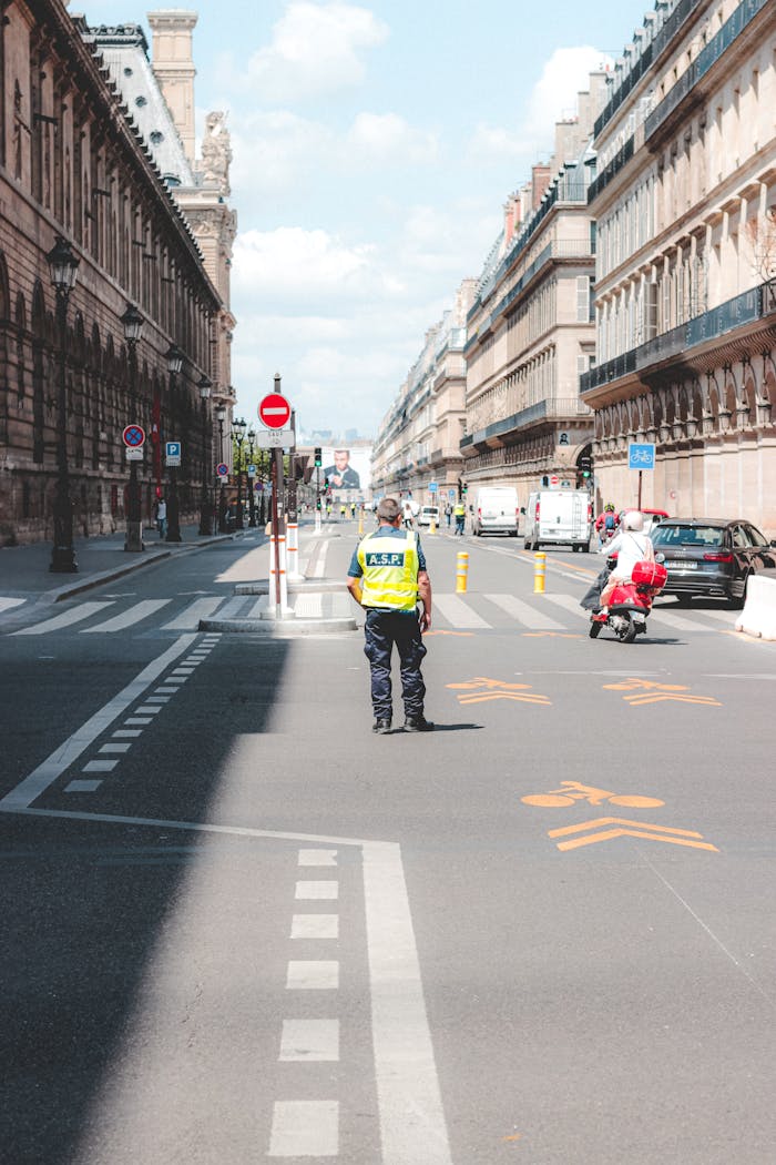 Traffic officer stands on a sunlit European street, directing vehicles and pedestrians.