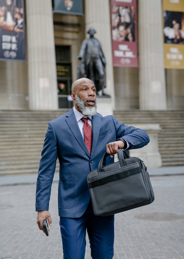 Bearded man in suit with briefcase walking outside a historic building.