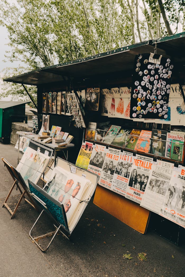Outdoor street stand displaying vintage posters, records, and buttons with trees in the background.